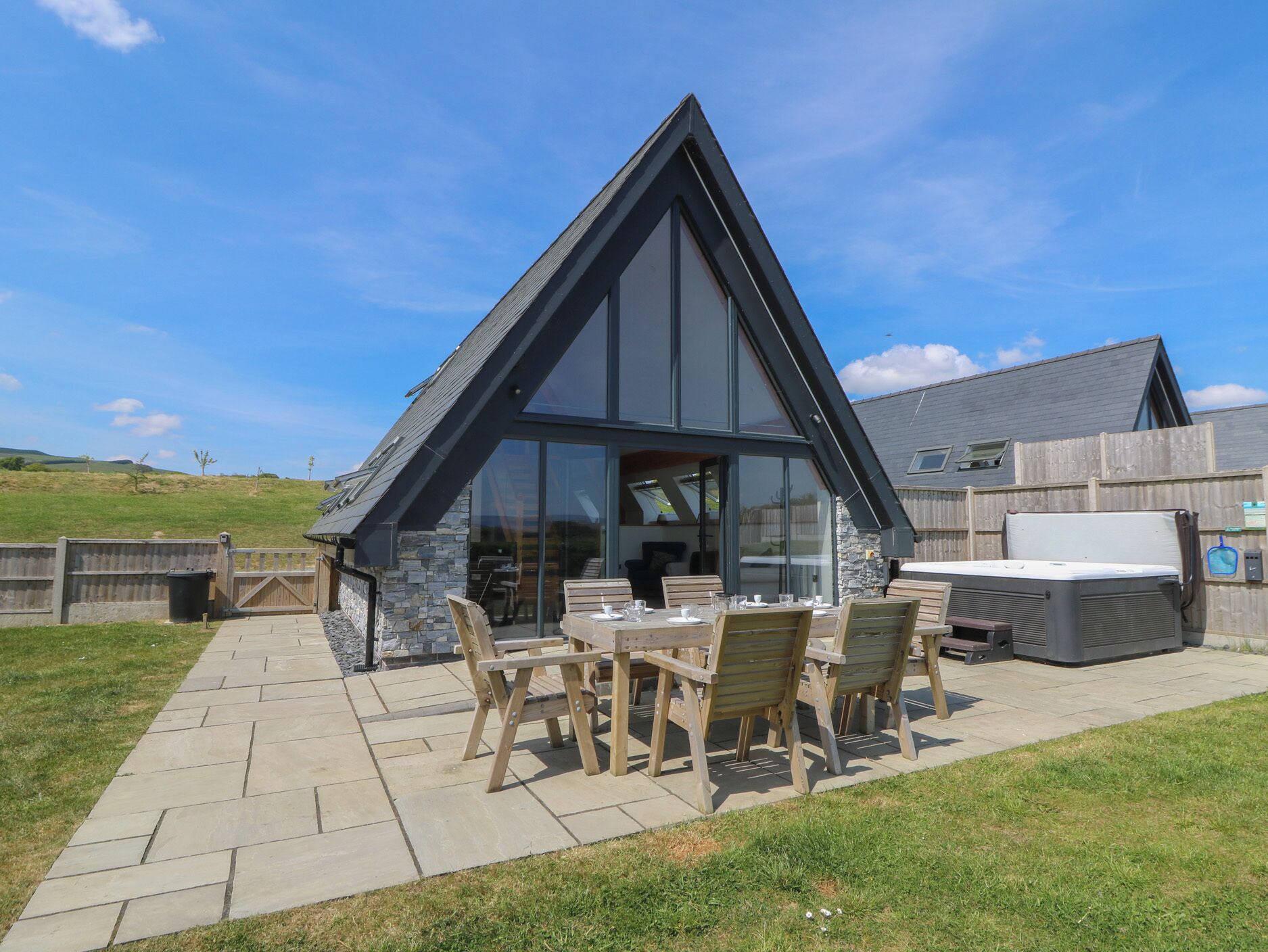 Ein modernes Haus mit Natursteinaußenwand und großen Fenstern, mit einer Terrasse, die einen Tisch und Stühle bietet.