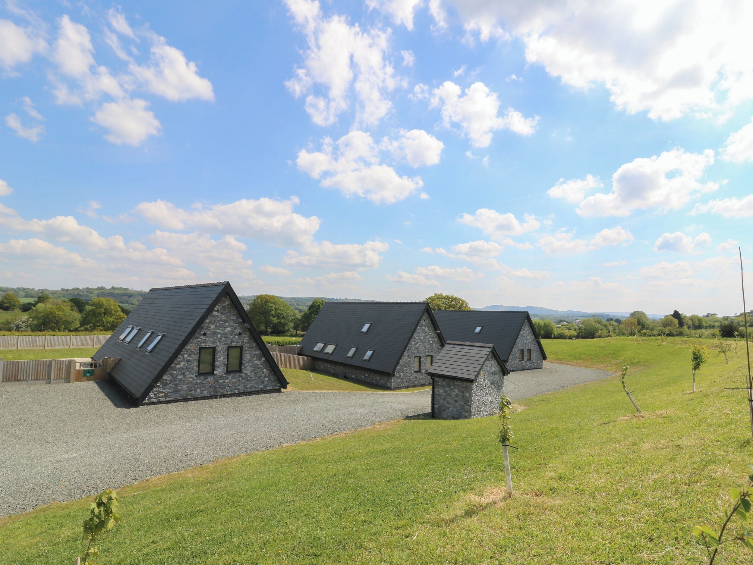 A row of three stone-roofed cottages with skylights, set in a grassy field with a clear sky.