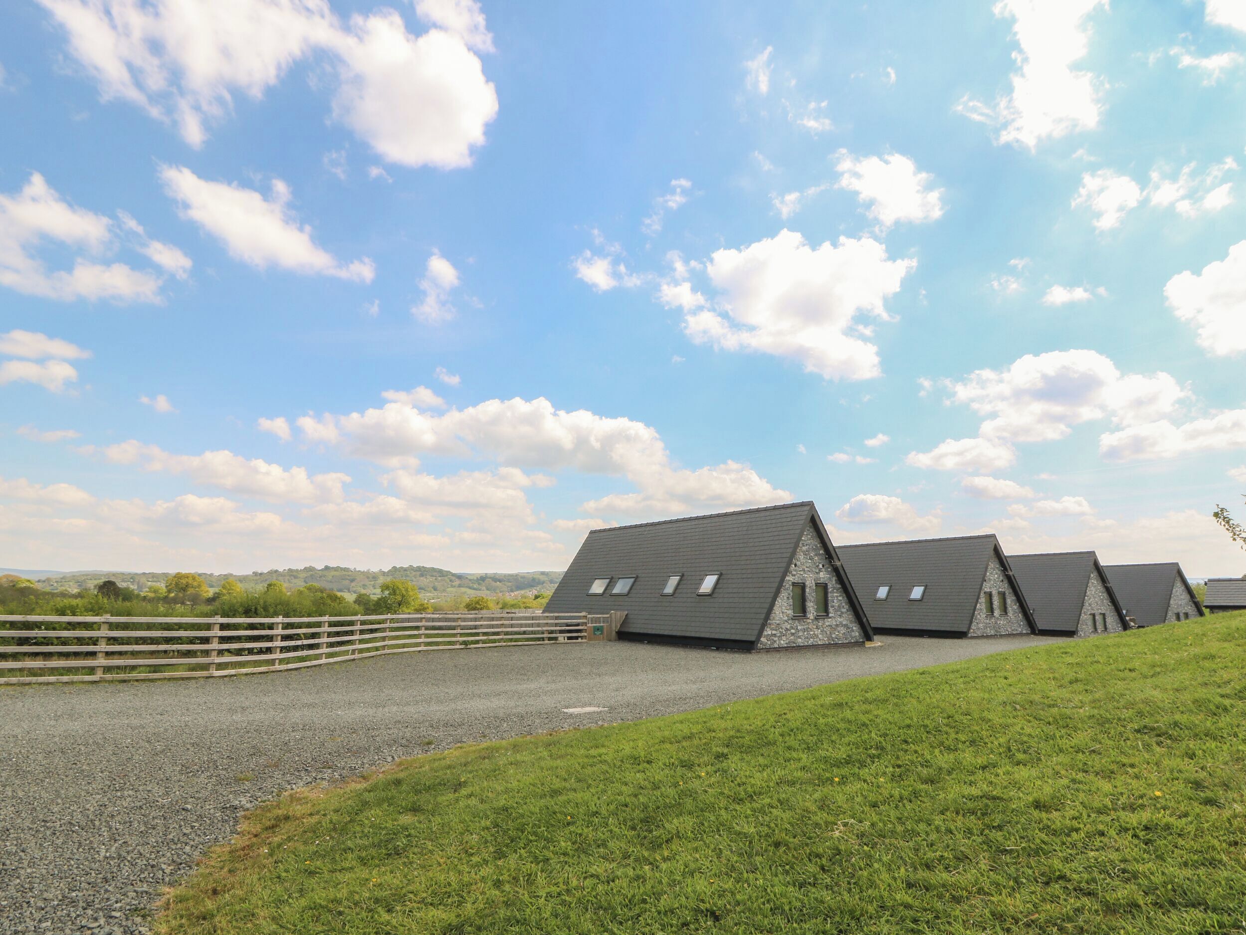 A row of modern, triangular-roofed buildings with a gravel driveway and a wooden fence.