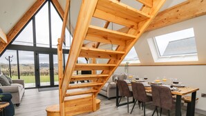 Moderni loft-tyylinen asunto, jossa on puinen portaikko, ruokailutila ja suuret ikkunat, joista avautuu näkymä maaseudulle.