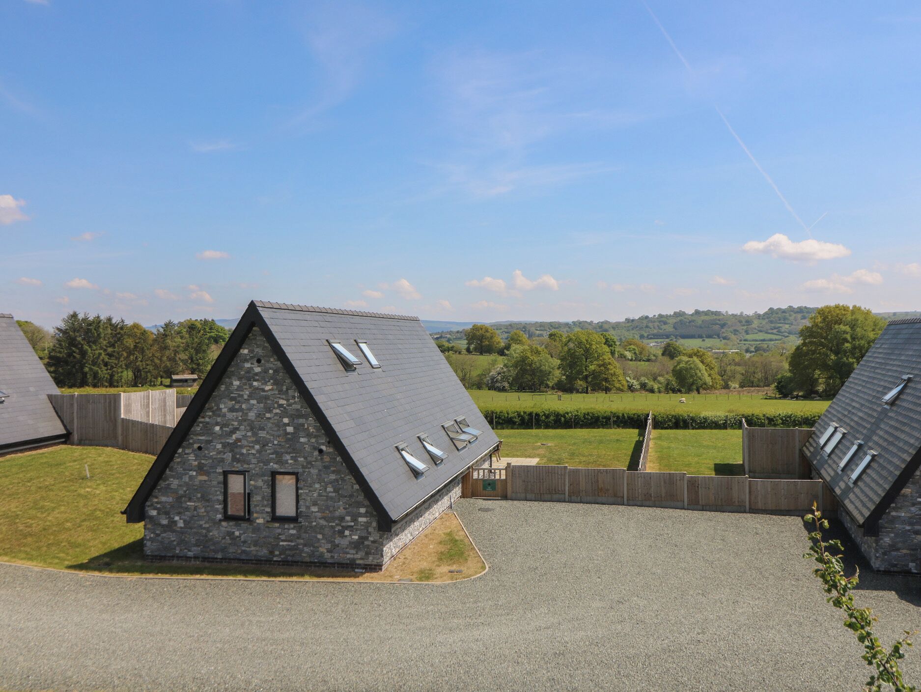 Ein modernes Haus mit geneigtem Dach und Oberlichtern, umgeben von einem eingezäunten Garten und einer malerischen Landschaft.