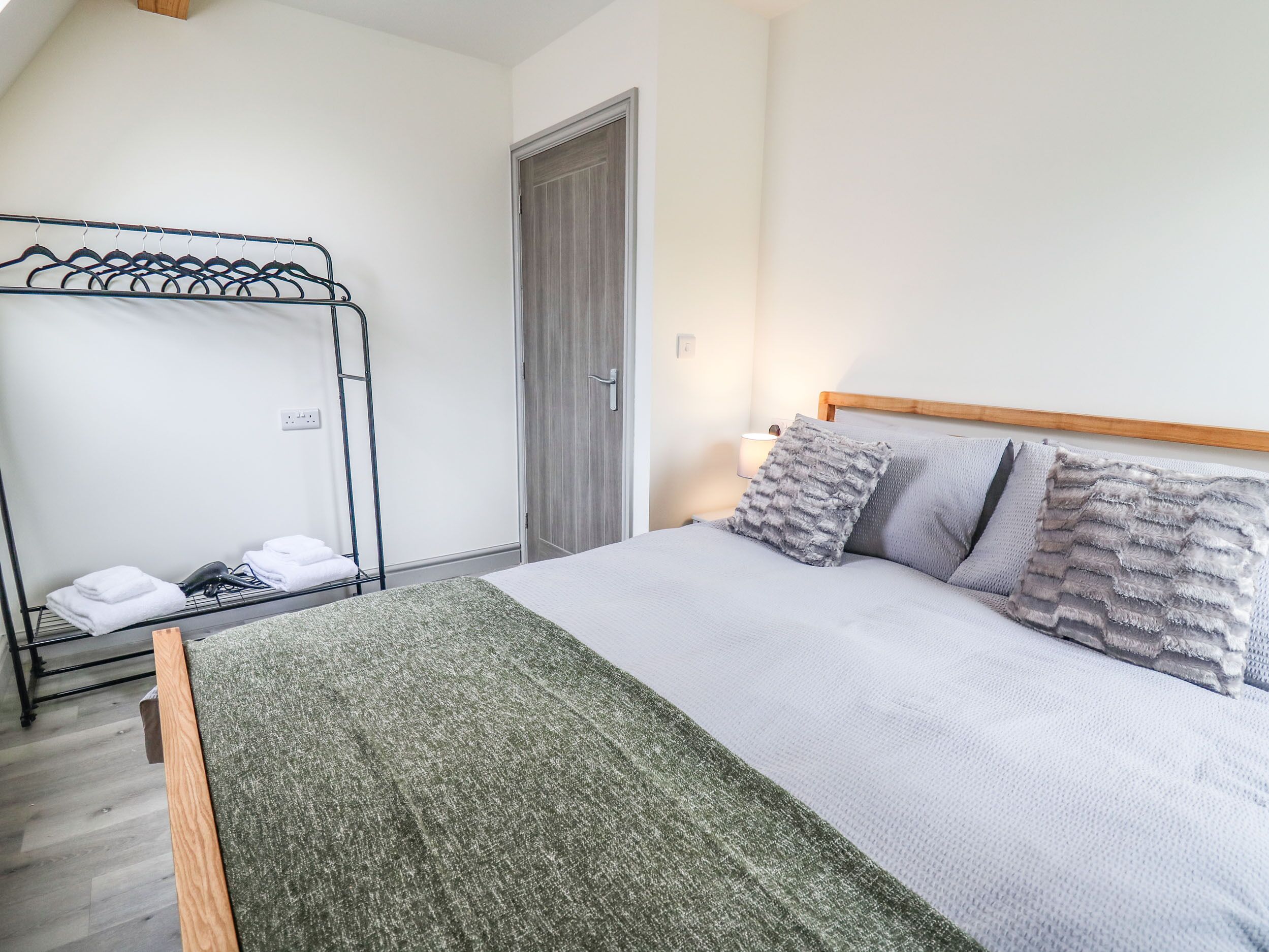 A bedroom with a bed, a wooden headboard, a grey blanket, and a grey pillow.