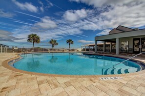 A swimming pool with a clear blue sky, palm trees, and a covered area with outdoor seating.