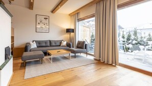 A modern living room with a grey sofa, a wooden coffee table, and a large window with curtains. - mit 2 Schlafzimmern by Interhome (Kitzbühel)