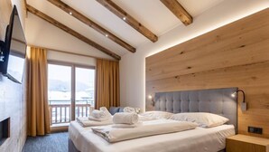 A hotel room with a large bed, wooden ceiling beams, a flat-screen TV, and a view of a snowy landscape. - mit 2 Schlafzimmern by Interhome (Kitzbühel)