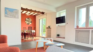 A modern living room with a dining area, large windows, and a TV mounted on the wall. - La Renaissance *** - Collection La 21ème Planche (Bayeux)