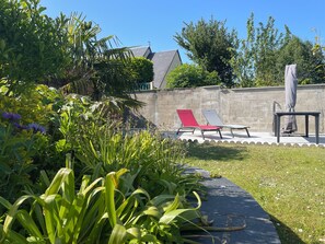 A garden area with a stone wall, two lounge chairs, and a table with an umbrella. - La Renaissance *** - Collection La 21ème Planche (Bayeux)