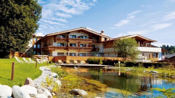 A multi-story hotel with balconies, a swimming pool, and a pond.