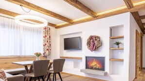 Ein modernes Wohnzimmer mit Holzboden, Kamin, Flachbildfernseher und Essbereich mit Tisch und Stühlen.