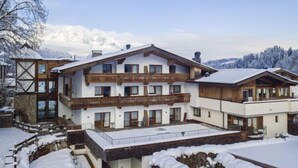 Un chalet à plusieurs étages, doté d’un balcon en bois, d’une entrée en pierre et surplombant un paysage enneigé.