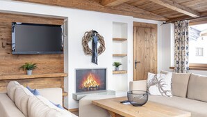 Un salon chaleureux avec un canapé, une table basse en bois, une cheminée, un téléviseur fixé à un mur en bois et une porte avec un cadre en bois.