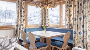 Un coin repas chaleureux avec une table et des chaises en bois, un vase rempli de fleurs et une vue sur un paysage enneigé par de grandes fenêtres.