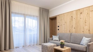 Een moderne woonkamer met een grijze bank, een houten dressoir en een groot raam met transparante gordijnen.