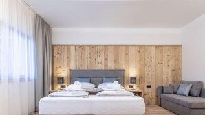 Een moderne slaapkamer met een houten paneelwand, een grijs bed met witte lakens, een grijze bank en twee bedlampjes.