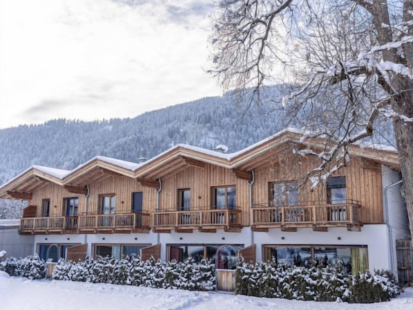 Un chalet en bois doté de plusieurs balcons, de grandes fenêtres et, en arrière-plan, d’un paysage enneigé.