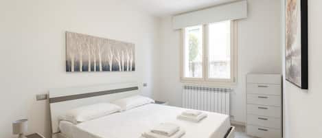 A bedroom with a bed, a nightstand, a dresser, a radiator, and a window.