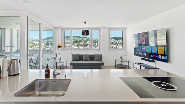 A modern kitchen with a large island, a flat-screen TV, and a sofa with a view of the city.
