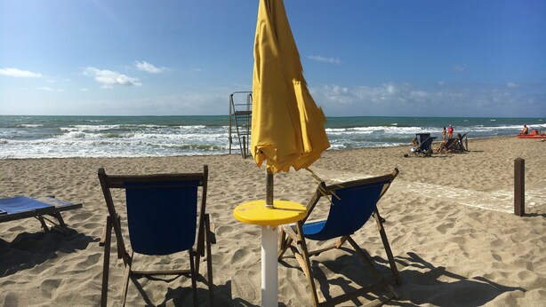 A beach with two blue lounge chairs and a yellow umbrella, a ladder, and a few people in the background. - COTTAGE WITH GARDEN AND PRIVATE BEACH (Castiglione della Pescaia)