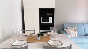 A dining area with a table set for two, a microwave, and a sofa in the background.