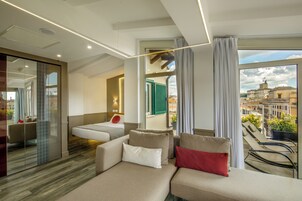 Una habitación de hotel moderna con sofá, cama, balcón con sillas y vista a la ciudad.