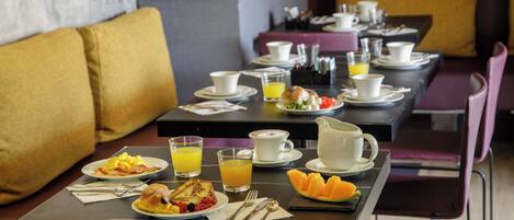A breakfast setting with a table set for two, including plates of food, cups, and a pitcher of orange juice.