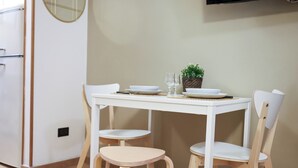Une petite table de salle à manger blanche, avec deux chaises, un bol, deux verres à vin et une petite plante posée sur la table.