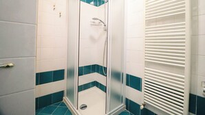 Une cabine de douche avec une porte en verre, des carreaux blancs et turquoise, et un radiateur blanc.
