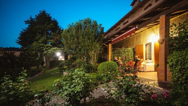 A well-lit garden area with a brick building, a dining area with outdoor seating, and a clear sky.