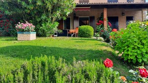 A house with a garden, a patio with a table and chairs, and a red awning over the entrance.