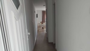 Un couloir avec un plancher en bois, des murs blancs et une porte sur le côté gauche.