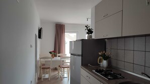 Une cuisine compacte équipée d’un réfrigérateur, d’une cuisinière et d’un évier. On y trouve également un coin repas avec une table et des chaises, ainsi qu’une fenêtre avec des rideaux.
