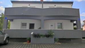 Un bâtiment à deux étages, doté d’un toit plat, d’un petit balcon et d’une plante en pot placée au premier plan.