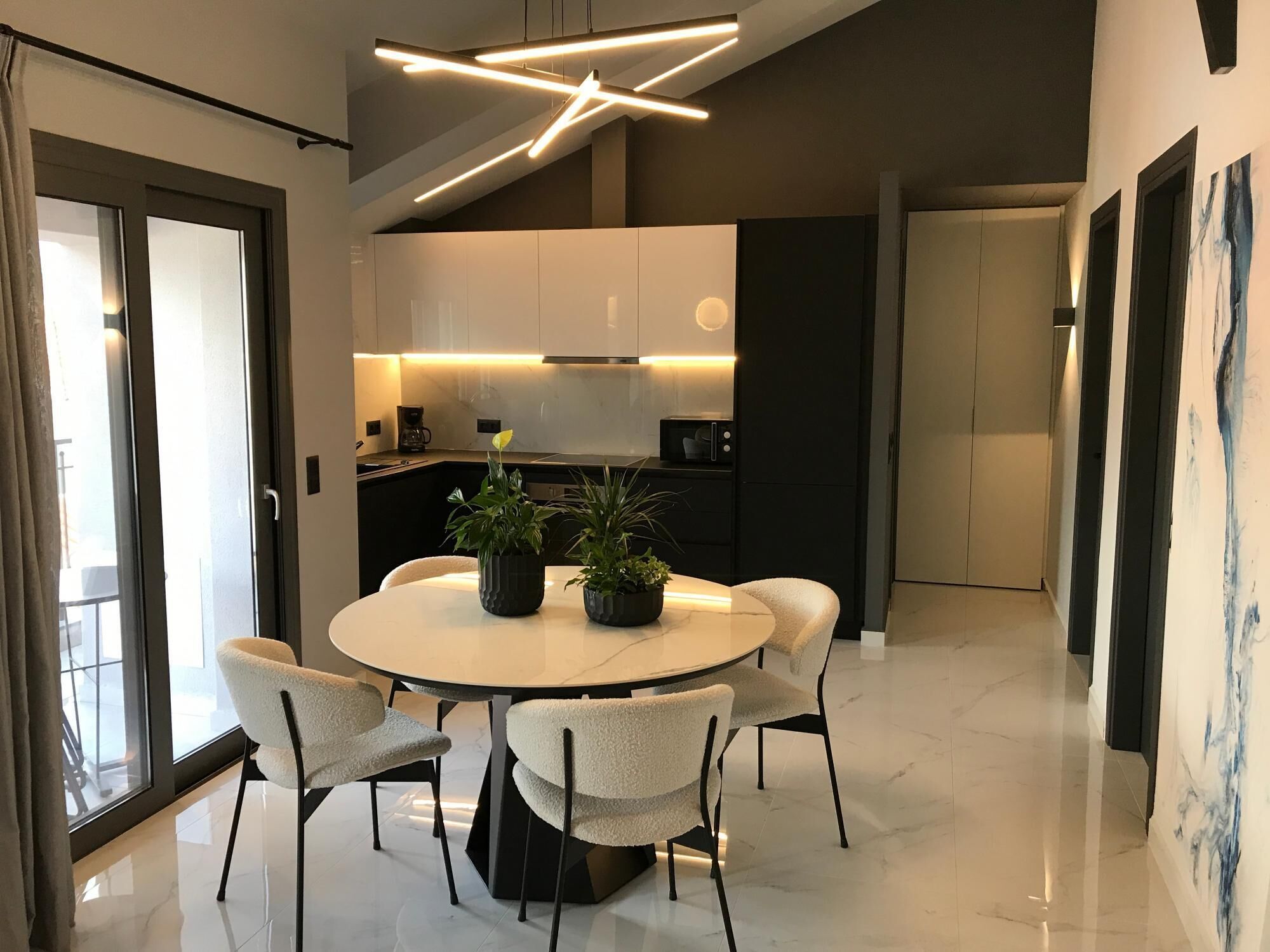 A modern dining area with a round table, four chairs, and two potted plants.