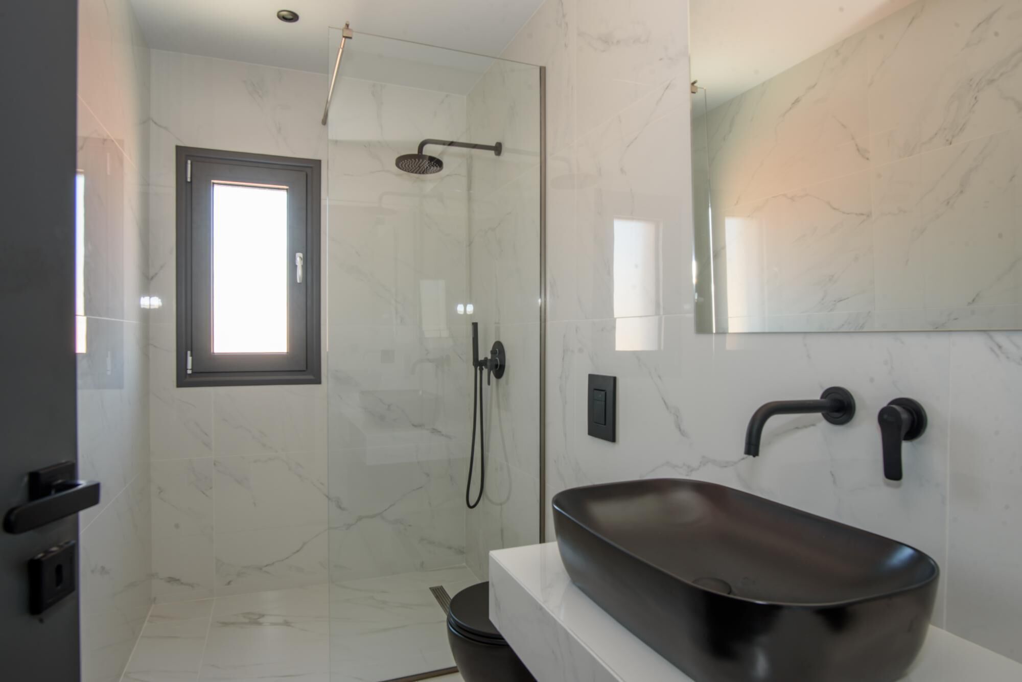 Ein modernes Badezimmer mit einer Glastrennwand zur Dusche, einem großen Spiegel und einem eleganten schwarzen Waschbecken.