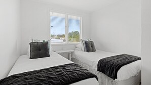 Une chambre avec deux lits, une fenêtre avec des stores et une petite table.