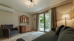 A modern bedroom with a large bed, a wooden dresser, a dark armchair, a floor lamp, and a sliding glass door leading to an outdoor area. - oDam Otel (Urla)