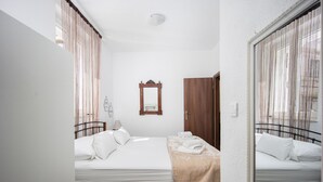 Een slaapkamer met twee bedden, een houten garderobe, een spiegel en een raam met gordijnen.