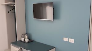 Una habitación moderna con una pared de acento color turquesa, un televisor de pantalla plana sobre un escritorio, una silla y un banco.