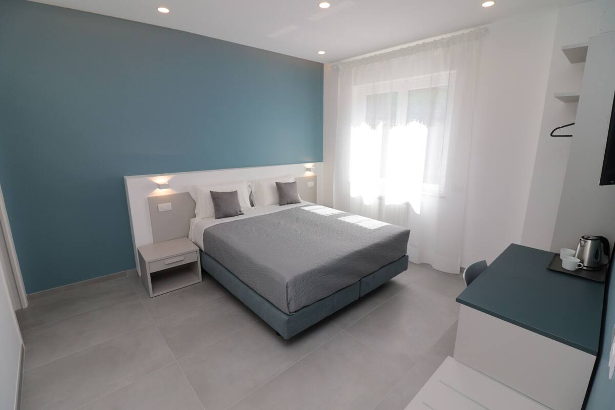 A modern bedroom with a bed, bedside tables, a small desk, and a window with curtains.