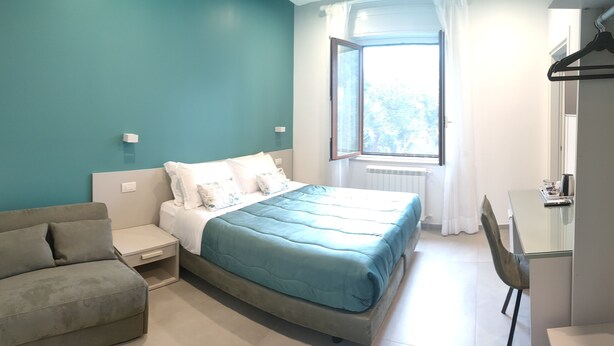 A bedroom with a bed, a nightstand, a sofa, a desk, and a window with curtains. - Maison Nanà (Sorrento)
