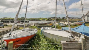A marina with several boats docked, a clear sky, and a distant view of a coastal village. - Tides Reach (Newton Stewart)