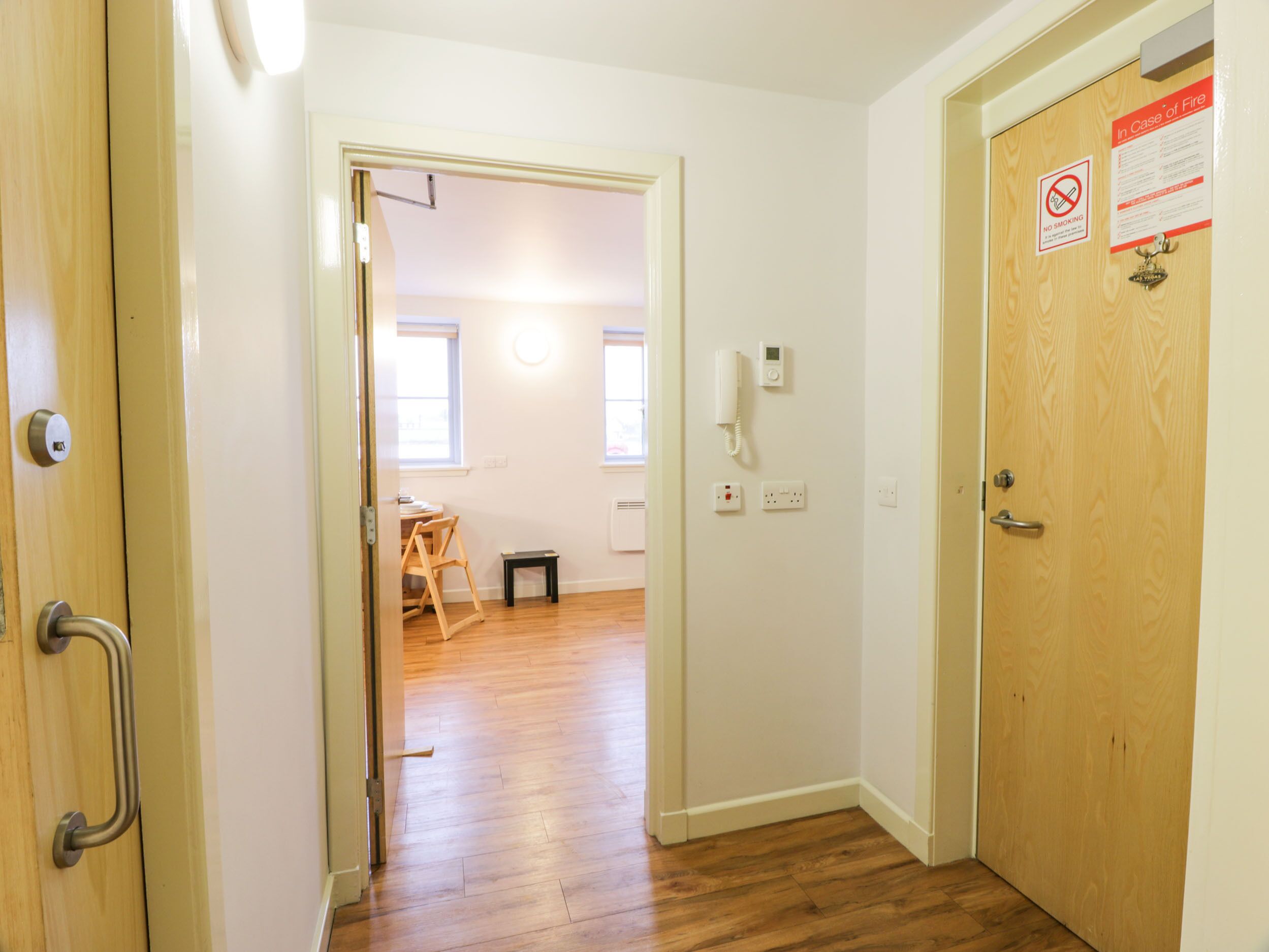 A hallway with a wooden door on the right, a no smoking sign, and a phone on the wall.
