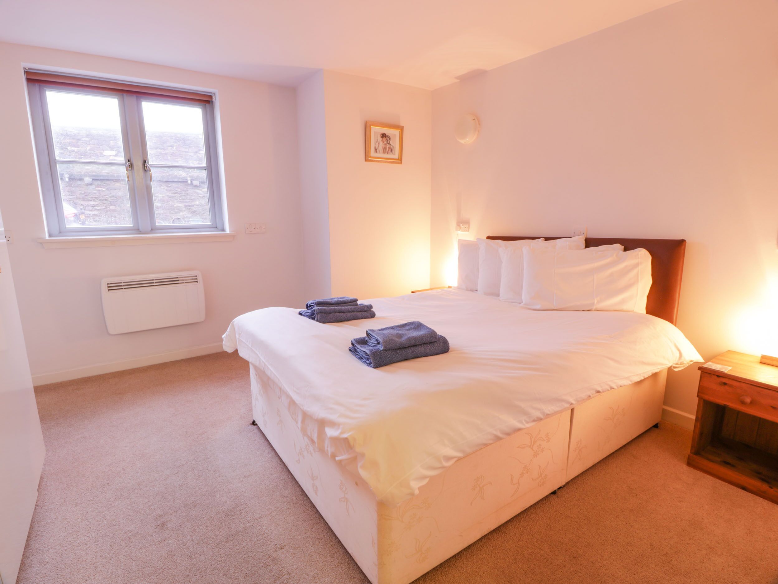 A bedroom with a large bed, a window, a radiator, and a bedside table.