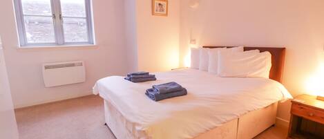 A bedroom with a large bed, a window, a radiator, and a bedside table.
