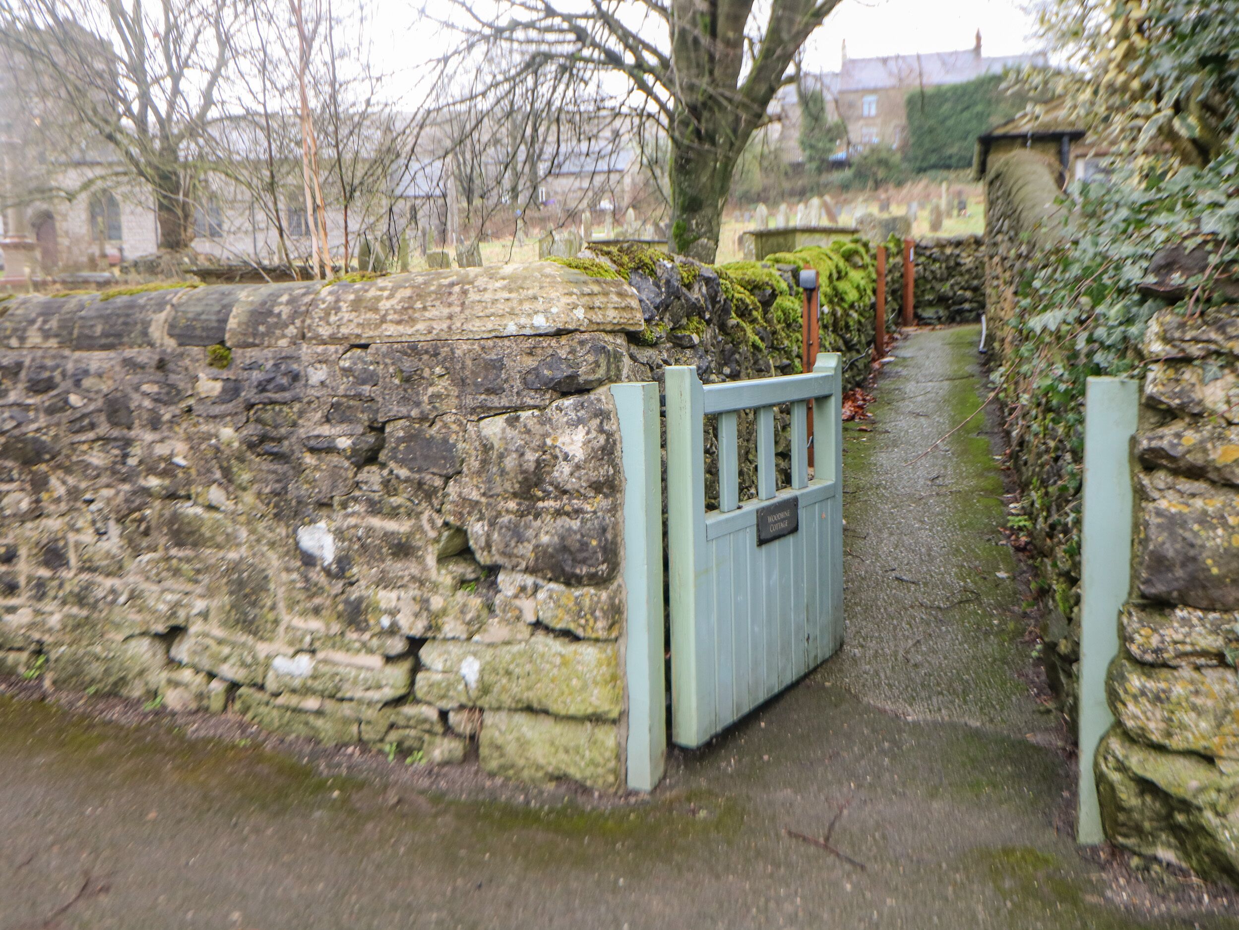 A stone wall with a metal gate, a narrow path, and a stone building in the background.