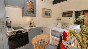 A compact kitchen with grey cabinets, a built-in oven, and a small dining area with a wooden chair and a table set for two.