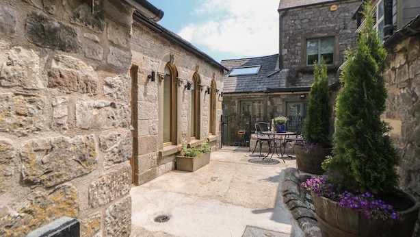 A stone courtyard with a table and chairs, surrounded by stone walls and potted plants.