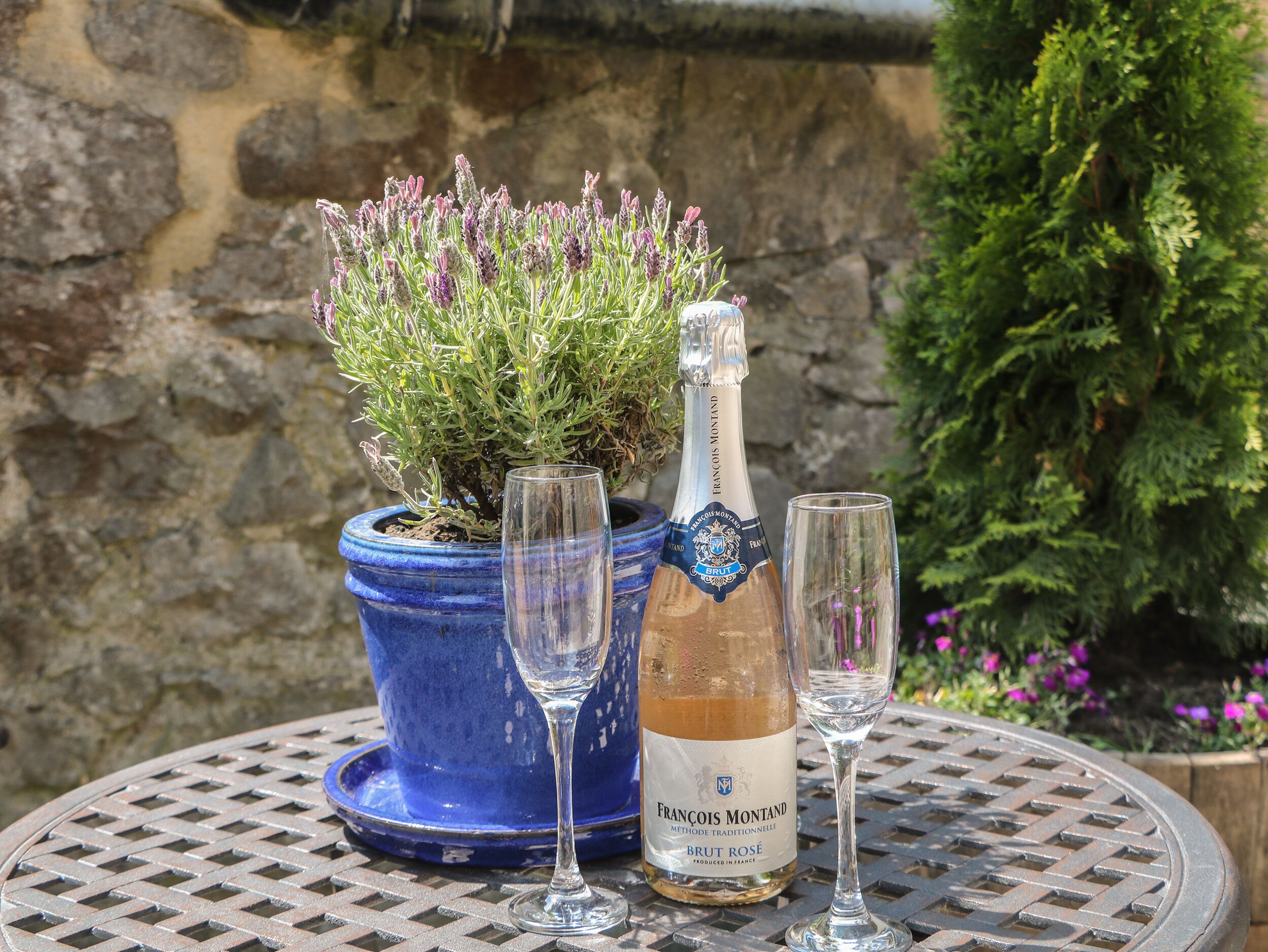 Eine Flasche Francois Montand Brut Rosé Wein, zwei Weingläser und ein Topf Lavendel auf einem Metalltisch.