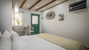 A bedroom with a bed, a desk, and a chair. There is a green door and a wall-mounted air conditioner.