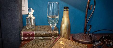 A table with a bottle of champagne, a glass, and a pair of glasses on a wooden surface against a blue wall.
